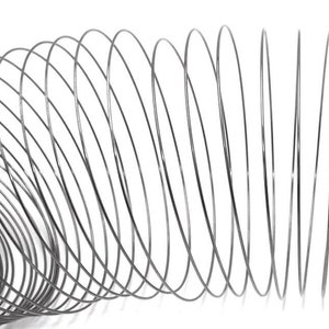 May include: A close-up of a coiled, metallic wire against a white background. The wire is a dark gray color and is arranged in a spiral pattern, creating a three-dimensional effect. The image is well-lit, highlighting the texture and form of the wire.