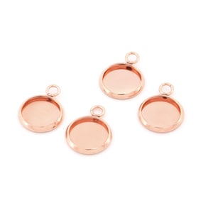 May include: Four rose gold-coloured round pendant trays with a small loop at the top for attaching to a chain or cord. The trays have a shallow, open design, ideal for creating custom jewellery.
