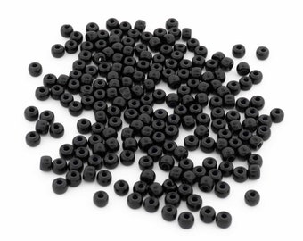 May include: A large pile of black seed beads, scattered on a white background.