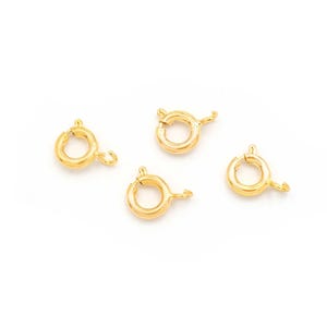 May include: Four gold-toned metal jump rings with a spring-loaded clasp. These rings are commonly used for jewellery making and crafting.