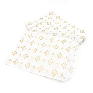 May include: A stack of white tissue paper with a gold geometric pattern. The paper is folded in half and the pattern is visible on both sides.