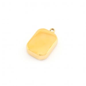 Pode incluir: Um pingente retangular dourado com cantos arredondados. O pingente tem uma pequena argola na parte superior para uma corrente. A superfície é lisa e reflexiva, com um acabamento brilhante e polido. O pingente é provavelmente feito de metal.