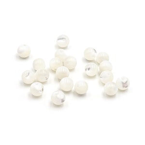 Peut inclure: Un ensemble de perles blanches et rondes avec un éclat nacré. Les perles sont dispersées sur une surface blanche, chacune présentant de subtiles variations de couleur et de texture. Idéales pour la création de bijoux et les projets d'artisanat.