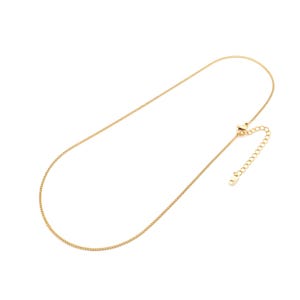 Peut inclure: Un collier à chaîne doré présentant un design délicat à maillons gourmette. Le collier comprend un fermoir mousqueton et une chaînette d'extension réglable avec plusieurs maillons circulaires plus larges à l'extrémité pour ajuster la longueur.