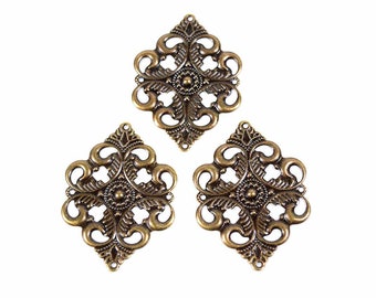 Puede incluir: Tres colgantes de filigrana de color latón antiguo. Cada colgante en forma de diamante presenta un diseño simétrico calado con motivos florales y de volutas. Tienen un pequeño lazo en la parte superior para la fijación, ideal para la creación de joyas o manualidades.