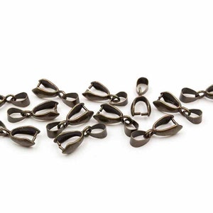 Könnte beinhalten: Eine Ansammlung von antik-bronze farbenen Schmuckverschlüssen, auf einer weißen Oberfläche verstreut. Jeder Verschluss hat eine Schlaufe und ein scharnierartiges, offenes Design, ideal für Halsketten oder Armbänder. Die Verschlüsse sind klein und haben eine detaillierte, Vintage-Ästhetik.