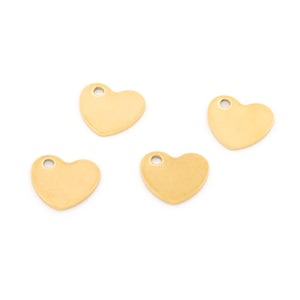 May include: Four small, flat, heart-shaped charms with a smooth, metallic gold finish. Each heart features a single circular hole near the top edge, designed for attachment to jewellery or other craft projects. The hearts are arranged in a scattered pattern.