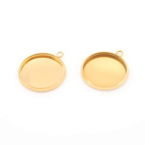 Könnte beinhalten: Zwei goldfarbene, runde Anhänger-Tabletts mit einer kleinen Schlaufe oben zum Befestigen an einer Kette oder einem Band. Die Tabletts haben eine flache, vertiefte Fläche zur Aufnahme eines Designs oder einer Verzierung. Die Anhänger sind vor weißem Hintergrund.