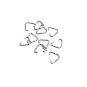 May include: A group of silver triangle-shaped metal rings, scattered on a white surface.
