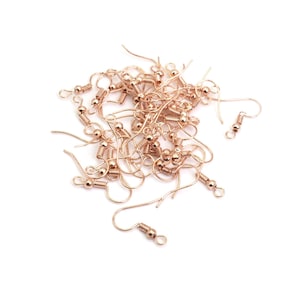 Könnte beinhalten: Ein Haufen goldfarbener Ohrhaken mit einer federbelasteten Verschlussschlaufe. Die Haken sind aus Metall und haben eine kleine Kugel am Ende.