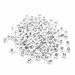 Può includere: Un mucchio di tessere di lettere bianche con lettere nere. Le tessere sono disposte in ordine casuale, con alcune lettere visibili.