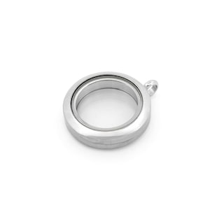 May include: A silver-colored, round locket with a clear glass center. The locket has a small loop at the top for attaching to a chain or other jewelry. The locket is made of a shiny, metallic material and is empty inside.