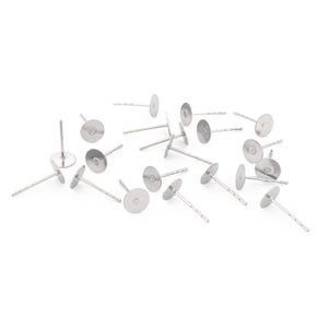 May include: A selection of silver earring posts, each with a flat, circular pad and a slender, straight post. The posts are arranged on a white surface, suitable for jewellery making.