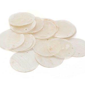 Può includere: Un mucchio di dischi bianchi, rotondi, a forma di conchiglia con fori al centro. I dischi sono disposti in modo casuale e sono tutti della stessa dimensione.