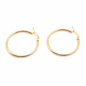 Könnte beinhalten: Ein Paar goldfarbene Creolen mit einer glatten, polierten Oberfläche. Jeder Ohrring besteht aus einem kreisförmigen Drahtdesign mit einem klappbaren Stiftverschluss an der Oberseite, der eine sichere Befestigung am Ohrläppchen ermöglicht.