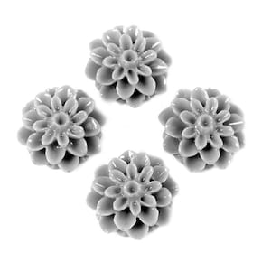 Puede incluir: Cuatro cabujones de resina gris en forma de flores con un centro elevado y múltiples pétalos.