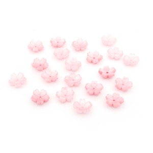Op de afbeelding: Een verzameling van 18 roze bloemvormige kralen, elk met een delicaat, licht verhoogd ontwerp. De kralen zijn verspreid over een witte achtergrond.