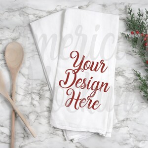 May include: Two folded white kitchen towels with the text "Your Design Here" in red script. Two wooden spoons are on the left, and a sprig of greenery with red berries is on the right.