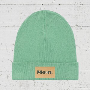 Könnte beinhalten: Eine hellgrüne Mütze mit einem braunen Lederflicken, auf dem "Mo"n." steht.