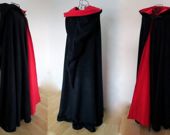 May include: A black hooded cape with a red lining. The cape is made of a soft, plush fabric and has a long, flowing design. The hood is large and can be pulled up over the head.