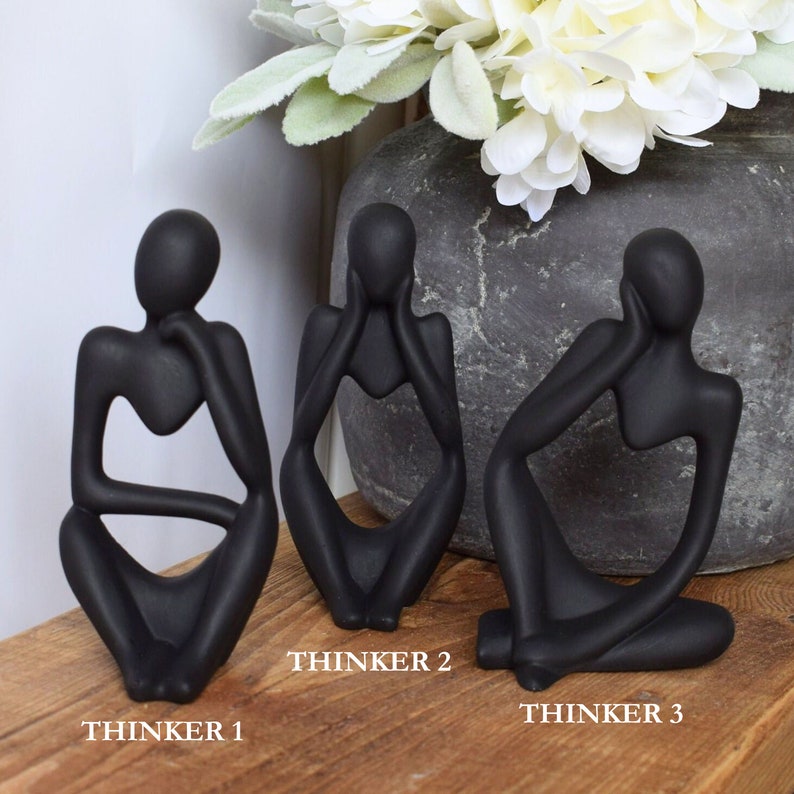 May include: Three black abstract sculptures of people sitting with their chins on their hands. The sculptures are labelled "Thinker 1", "Thinker 2", and "Thinker 3".