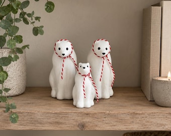 May include: Three white polar bear figurines in varying sizes, each featuring a smooth matte finish, black painted eyes and noses, and a decorative red and white baker's twine tied around their necks in a simple bow.