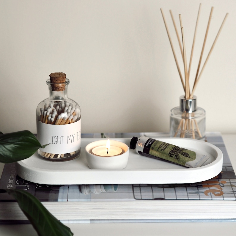 Puede incluir: Bandeja ovalada blanca con un frasco de vidrio lleno de cerillas, una peque&ntilde;a vela blanca y un tubo de crema de manos. El frasco tiene una etiqueta que dice "Light My Fire".