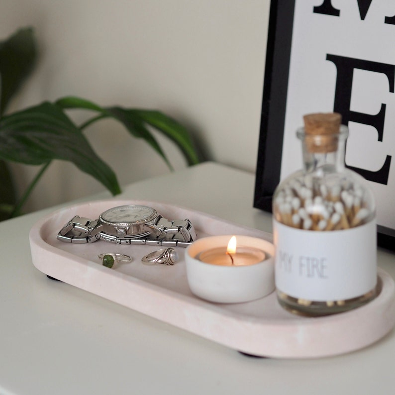 Puede incluir: Una bandeja ovalada rosa con un reloj, anillos, una peque&ntilde;a vela blanca y un frasco de vidrio lleno de cerillas. El frasco tiene una etiqueta que dice "My Fire".