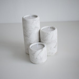 May include: Three white marble candle holders of different sizes. The candle holders are cylindrical and have a marbled pattern.