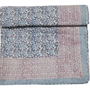 Peut inclure: Une courtepointe en coton blanc avec un motif floral bleu et violet. La courtepointe a une bordure avec un motif géométrique dans des tons de rose et de bleu.