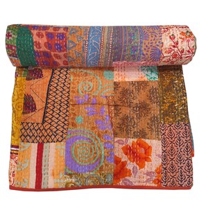 Peut inclure: Une courtepointe patchwork enroulée avec une bordure rouge. Elle est composée de carrés et de rectangles aux tons orange, marron, bleu et violet. Des motifs floraux et géométriques sont visibles. Différents tissus composent la courtepointe.