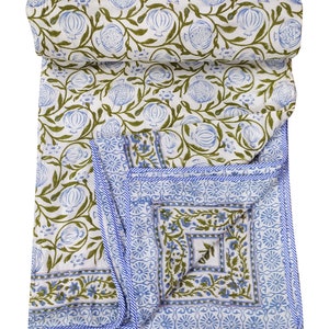 May include: A white cotton quilt with a blue and green floral pattern. The quilt is folded in half and has a blue border.
