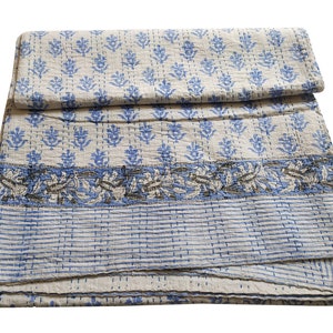May include: A white and blue kantha quilt with a floral pattern. The quilt is folded in half and has a striped border.