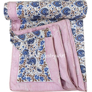 May include: A white cotton quilt with a blue and brown floral print. The quilt has a pink and white striped border with a brown stitched edge.