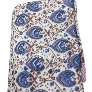 May include: White cotton fabric with a blue and brown floral print. The fabric is folded in half and has a pink and white striped border.