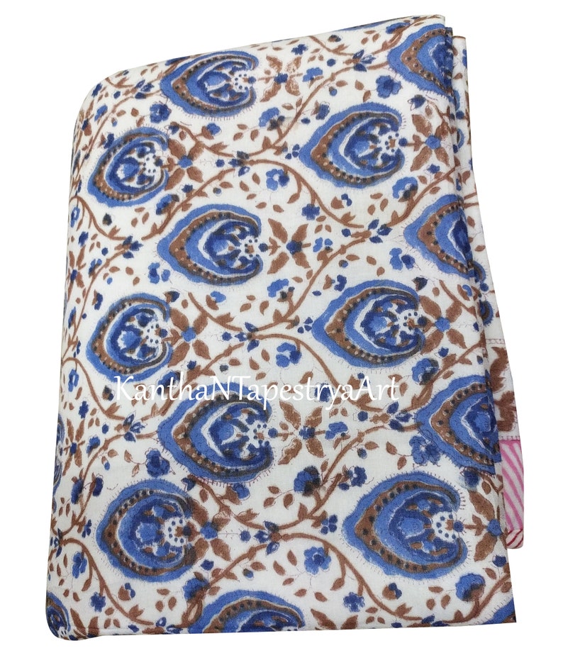 May include: White cotton fabric with a blue and brown floral print. The fabric is folded in half and has a pink and white striped border.