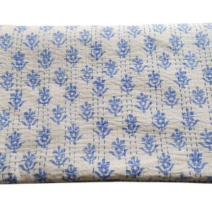 May include: A white cotton quilt with a blue floral pattern. The quilt is folded in half and has a subtle texture.
