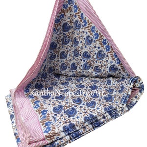 May include: A white cotton quilt with a blue and brown floral pattern. The quilt has a pink and white striped border. The quilt is folded in thirds and is lying on a white background.