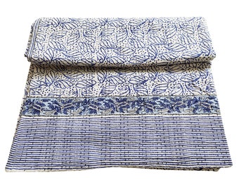 Könnte beinhalten: Eine weiße und blaue Baumwolldecke mit einem Blumenmuster und einem gestreiften Rand. Die Decke ist in der Mitte gefaltet und hat eine strukturierte Oberfläche.
