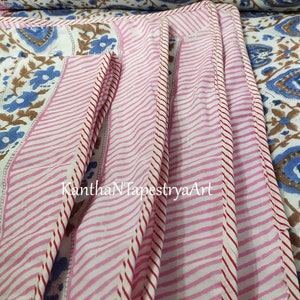 May include: Close-up of a pink and white striped fabric with red stitching. The fabric has a floral pattern and the text "KanthaNTapestryaArt" is visible.