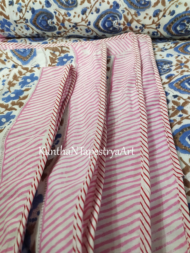 May include: Close-up of a pink and white striped fabric with red stitching. The fabric has a floral pattern and the text "KanthaNTapestryaArt" is visible.