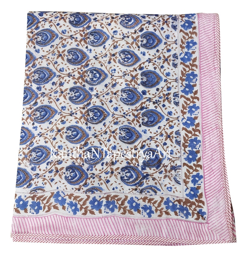 May include: White cotton throw blanket with a blue and brown floral pattern. The blanket has a pink and white striped border.