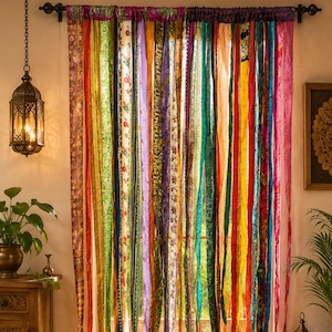 Peut inclure: Un rideau de fenêtre composé de nombreuses bandes de tissu verticales aux couleurs et motifs variés, notamment rouge, vert, jaune, bleu, violet et orange. Les bandes sont suspendues à une tringle horizontale et tombent jusqu'au sol.