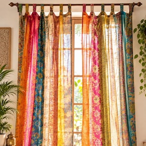 Pode incluir: Um par de cortinas de comprimento total com painéis verticais em tons vibrantes de laranja, rosa choque, azul-petróleo e amarelo. O tecido apresenta padrões florais e paisley intrincados, com alças superiores penduradas numa vara escura.