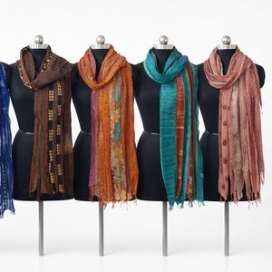 Peut inclure: Six écharpes colorées présentées sur des mannequins noirs. Les écharpes présentent des motifs variés, notamment des rayures et des motifs floraux. La palette de couleurs comprend le bleu, le marron, l'orange et le rose. Chaque écharpe est drapée autour du cou du mannequin.