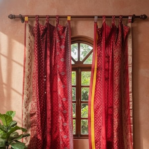 Puede incluir: Cortinas rojas estampadas con una franja amarilla cuelgan frente a una ventana. Una alfombra redonda de yute está sobre el suelo de madera. También se ven una planta en maceta y un pequeño taburete de madera con libros y una taza.