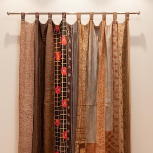 Pode incluir: Um conjunto de cortinas decorativas com uma variedade de tecidos estampados em tons de castanho, bege e dourado. As cortinas penduram de uma barra prateada e apresentam desenhos florais e geométricos.