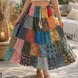 Könnte beinhalten: Maxirock im Patchwork-Stil mit Kordelzug in der Taille. Der Rock hat eine Vielzahl von gemusterten Stoffquadraten in Rot-, Blau-, Gelb- und Grüntönen. Das Model trägt ein weißes Crop-Top und braune Sandalen. Der Rock ist im Bohème-Stil.