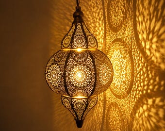 May include: A hanging pendant lamp with a metallic, onion-shaped body featuring intricate, laser-cut geometric patterns. The lamp emits a warm, golden light, casting detailed, circular shadow projections onto the adjacent wall surface.