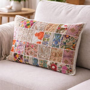 May include: A rectangular cushion with a patchwork design. The cushion displays a variety of colourful fabric squares with floral, paisley, and geometric patterns. It is placed on a light-coloured sofa.